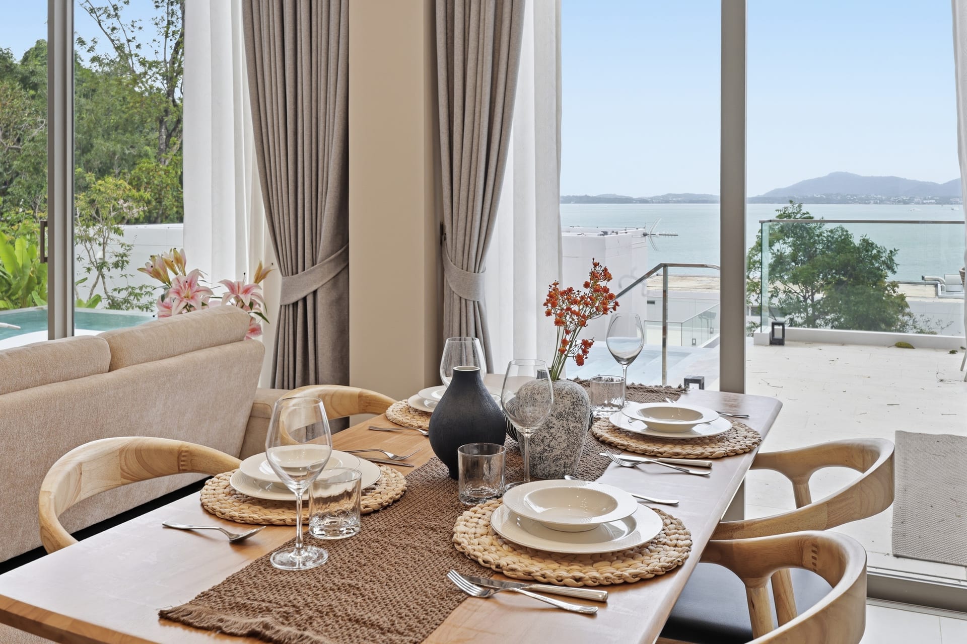 The dining table set for four in daylight with the Andaman Sea filling the floor-to-ceiling windows behind