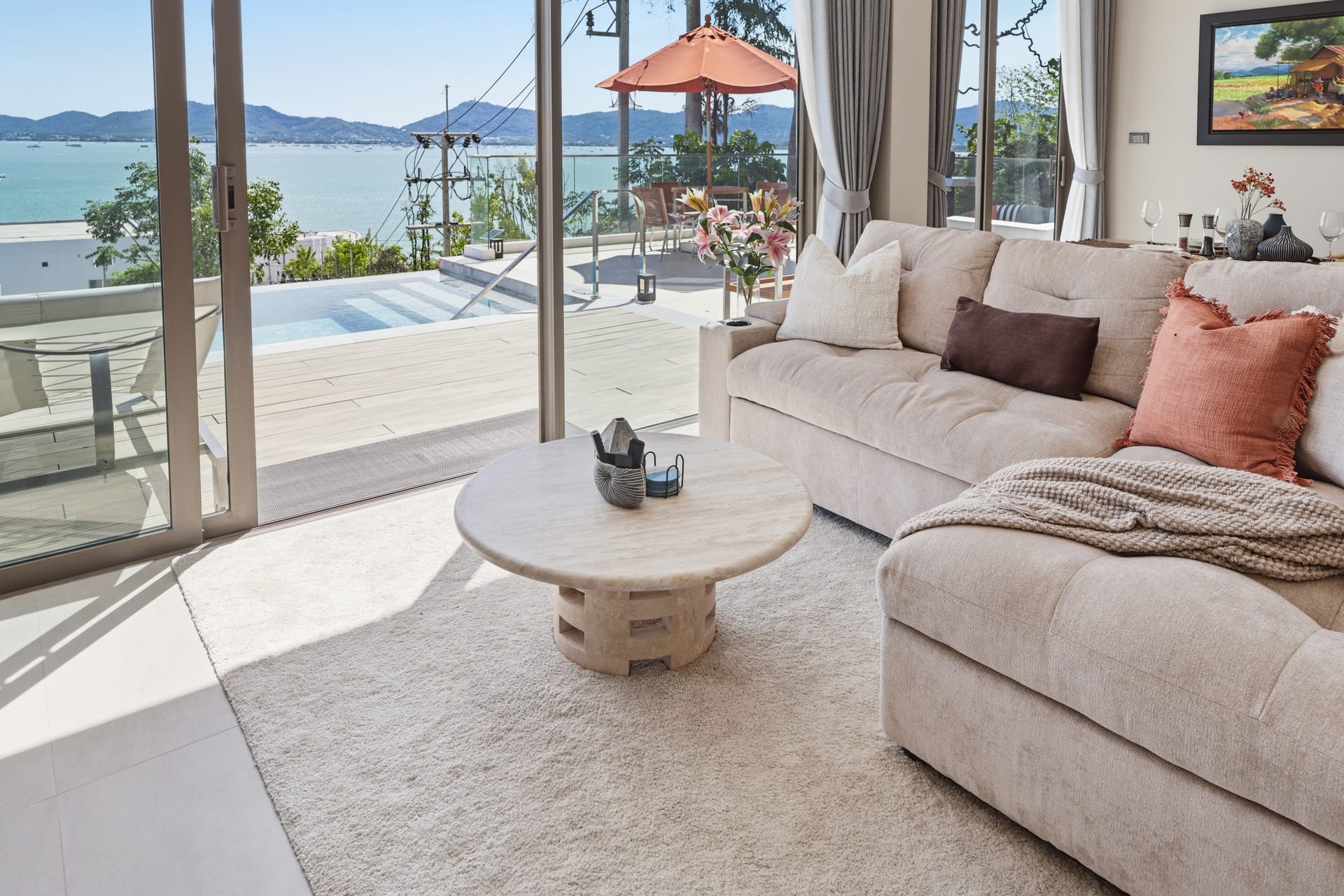 The great room with sliding doors open to the pool terrace and bay on a bright day, an orange parasol visible outside