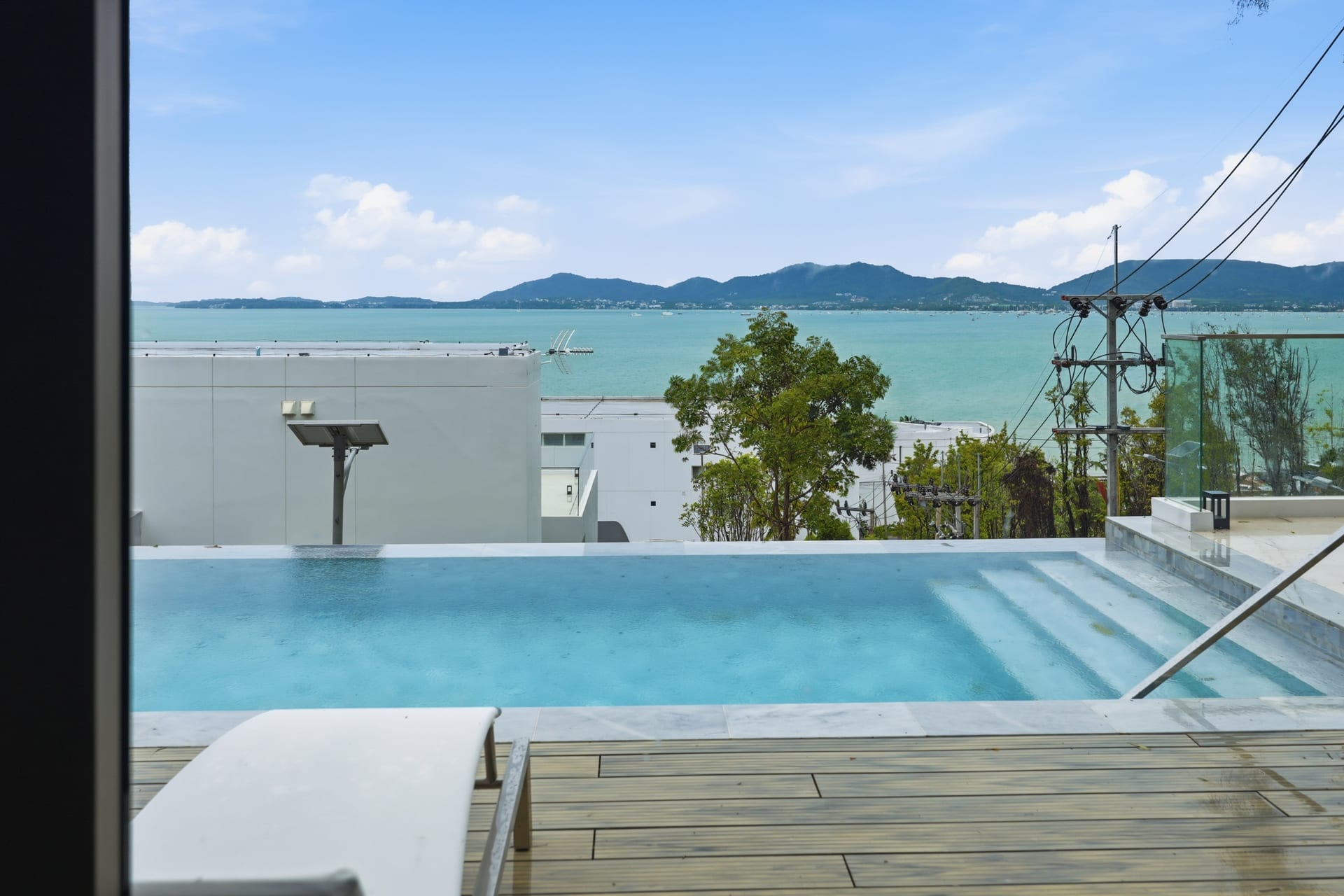 The infinity pool's edge dropping straight to the Andaman Sea on a sunny day, the bay and distant headlands beyond under a clear blue sky