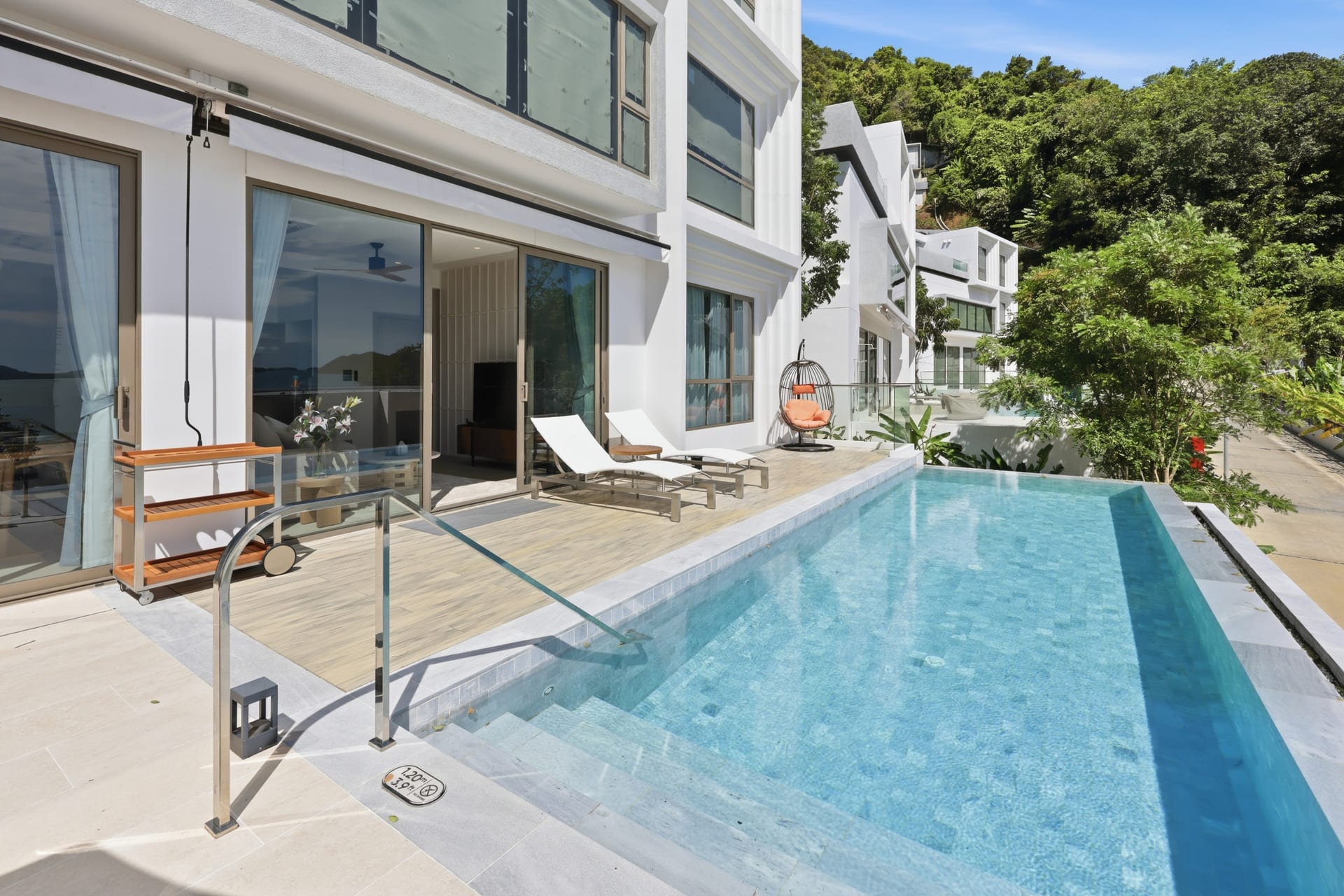 The infinity pool and the white villa terraces in full sun, loungers on the timber deck and the bay opening to the horizon