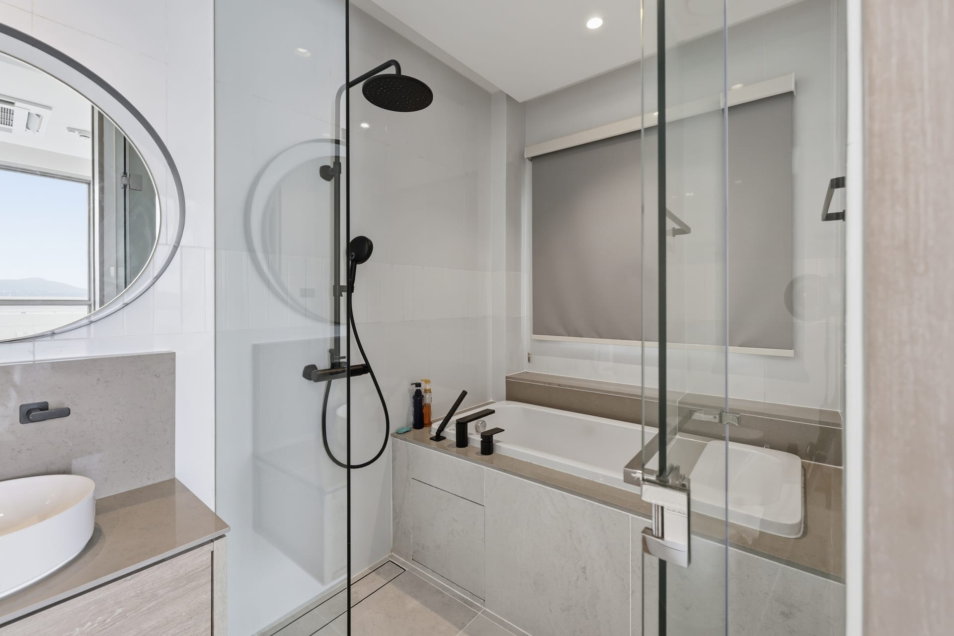 The primary bathroom's walk-in rainfall shower behind glass, stone tiling and a daylight window
