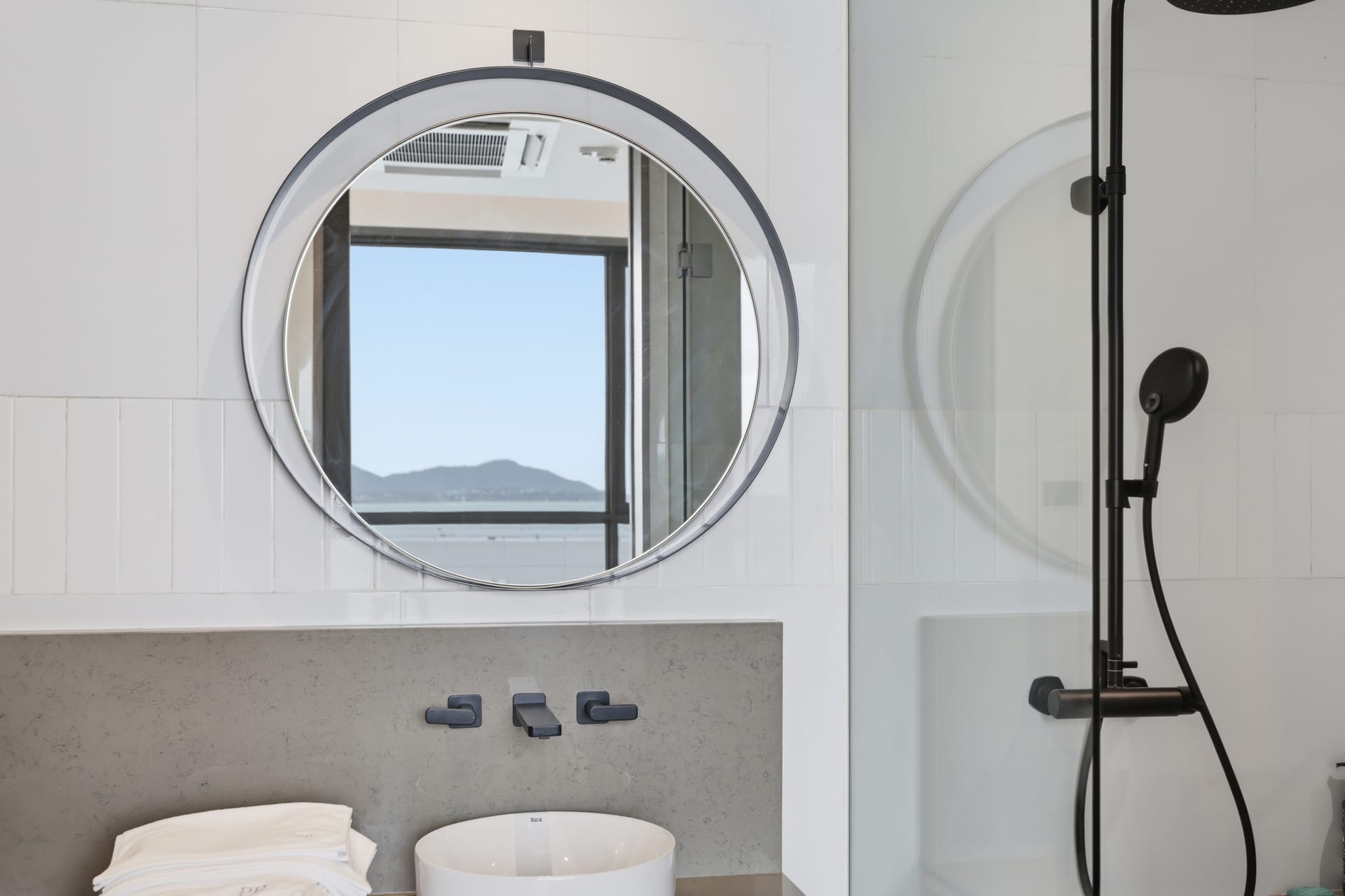 The second bathroom with a glass walk-in shower and round mirrors over the vanity, bright and clean